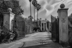 Entrée d'une villa de luxe abandonnée à Beverly Hills, grilles en fer forgé et haies envahissantes