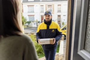 Facteur La Poste livrant un colis Colissimo devant une maison en zone résidentielle le matin